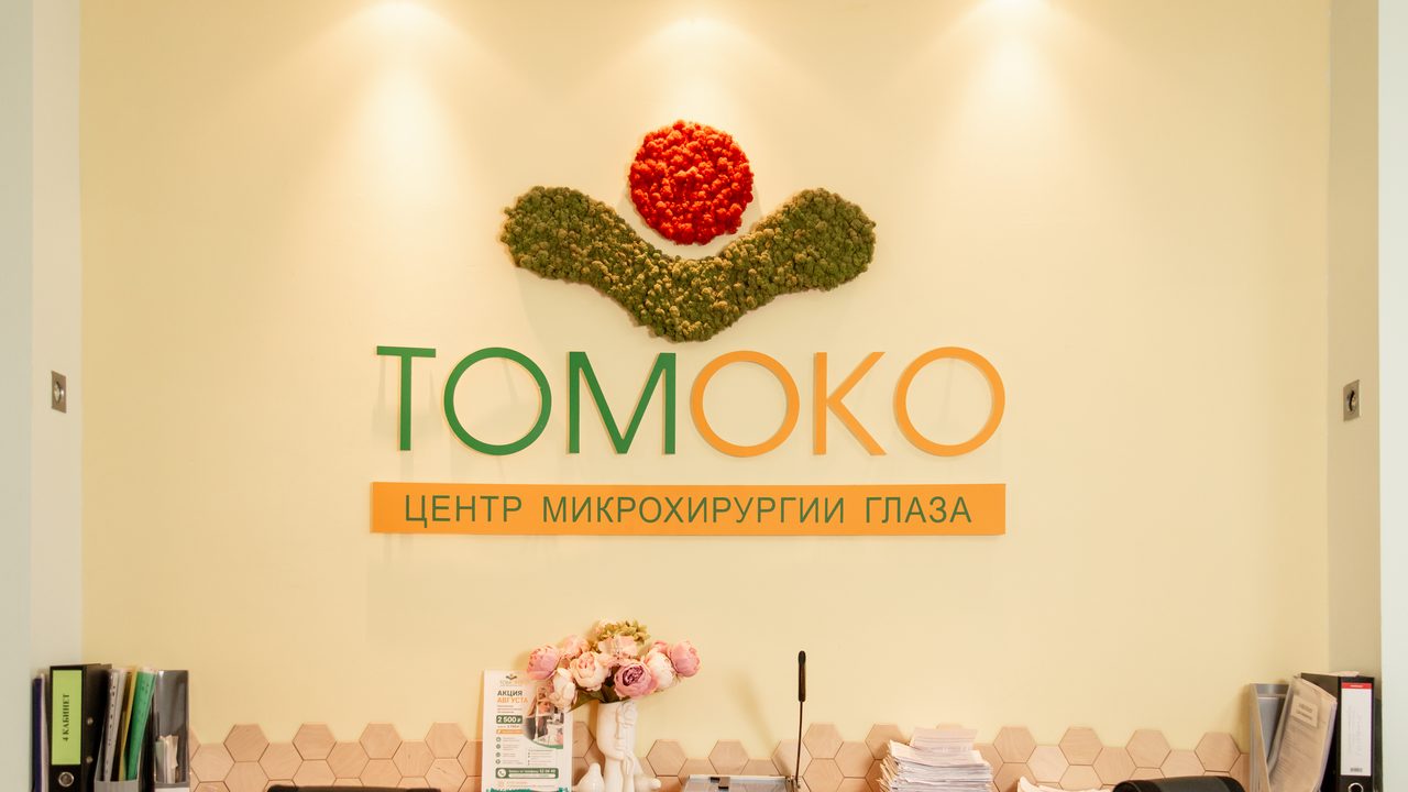 Ресепшен центра «ТомОко»: стена с логотипом и надписью «Центр микрохирургии глаза», стойка администратора